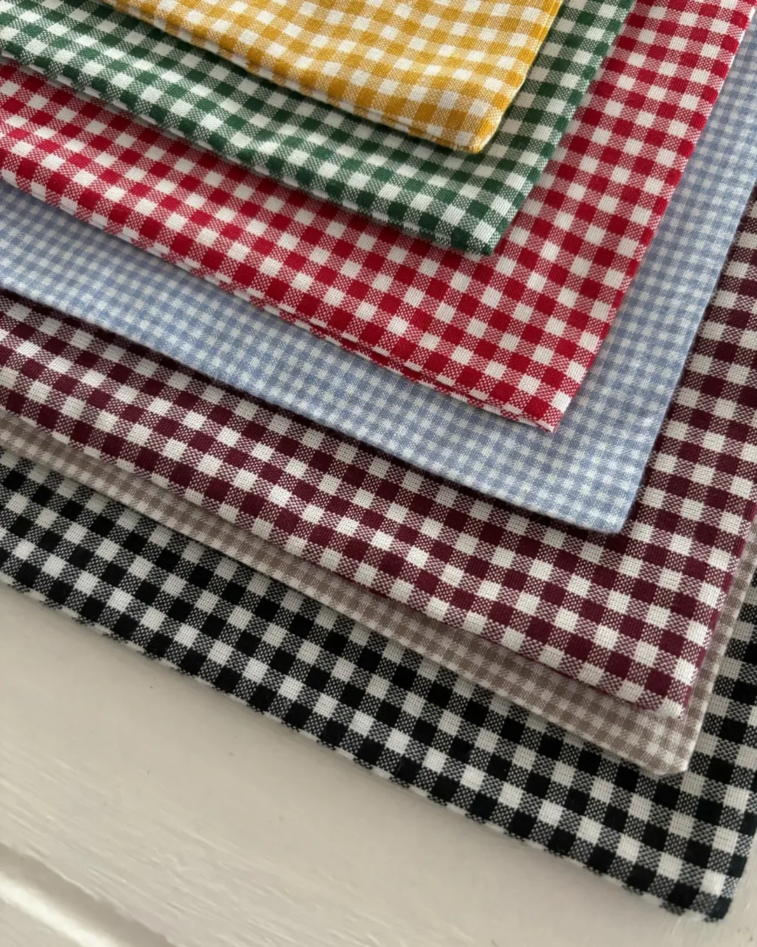 A variety of 100% locally woven cotton gingham fabrics for the Frenchy Tote in yellow, green, red, light blue, maroon, beige, and black.