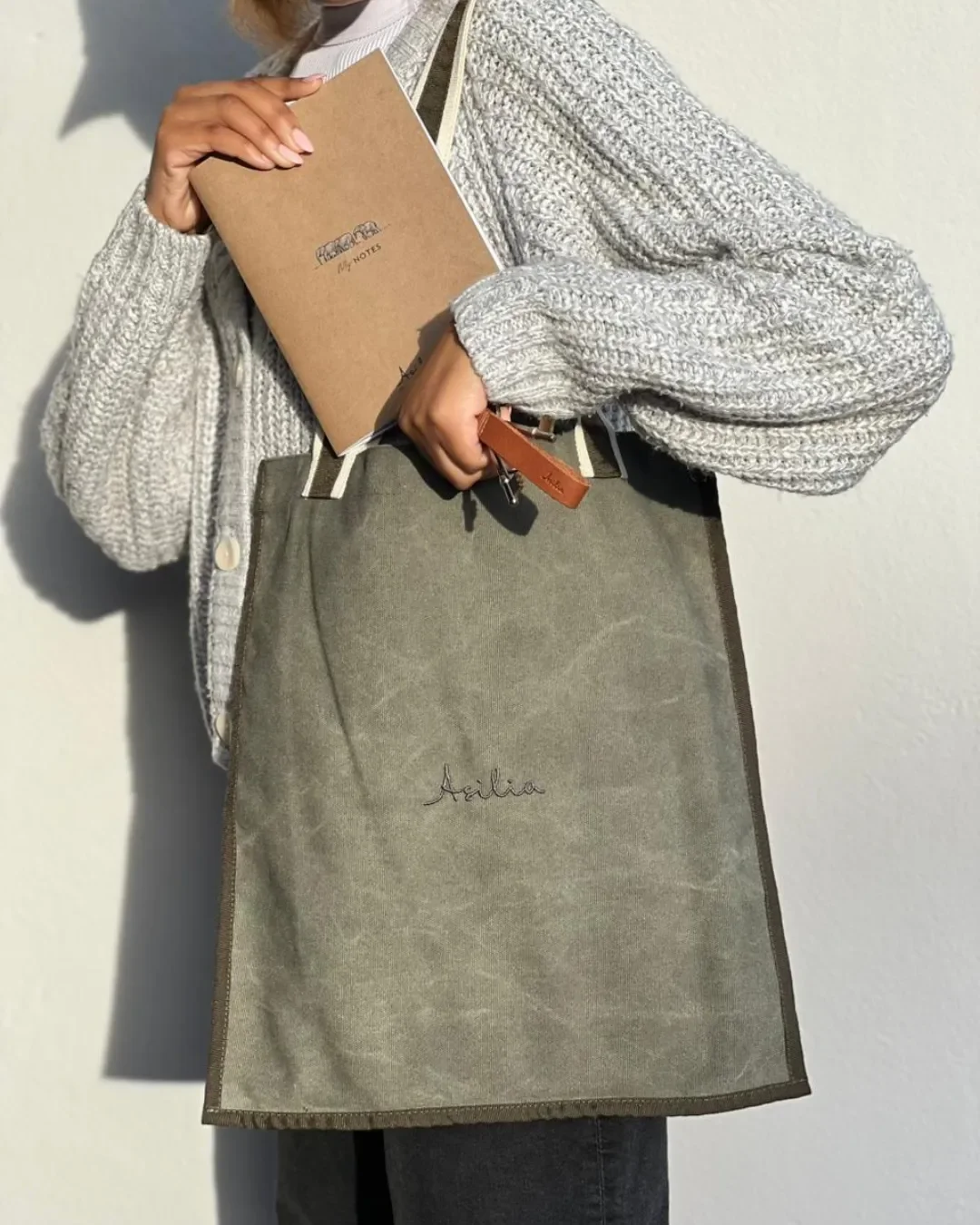 Close-up of a custom sustainable olive green tote bag and notebook, quality corporate merchandise handmade by local artisans at Soli Cape Town for Asilia.