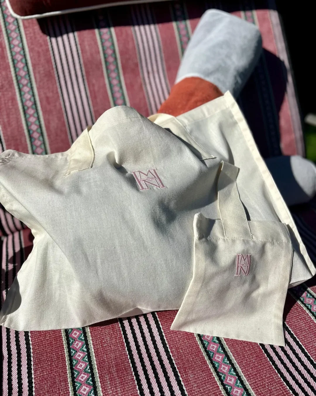 A set of small and large Mount Nelson gift bags in light natural calico fabric with pink embroidered MN logos, Handmade by Soli in Cape Town for sustainable merchandise or corporate gifts.