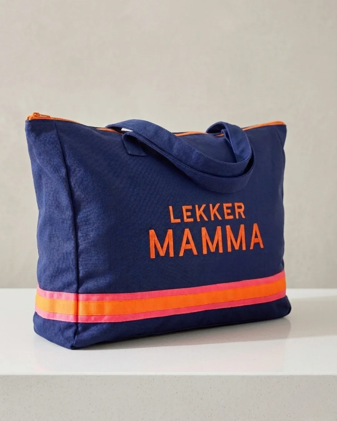 A navy blue k-sheeting tote bag featuring orange "Lekker Mamma" embroidery and bright orange and pink stripes, handmade by Soli in Cape Town for sustainable retail merchandise.