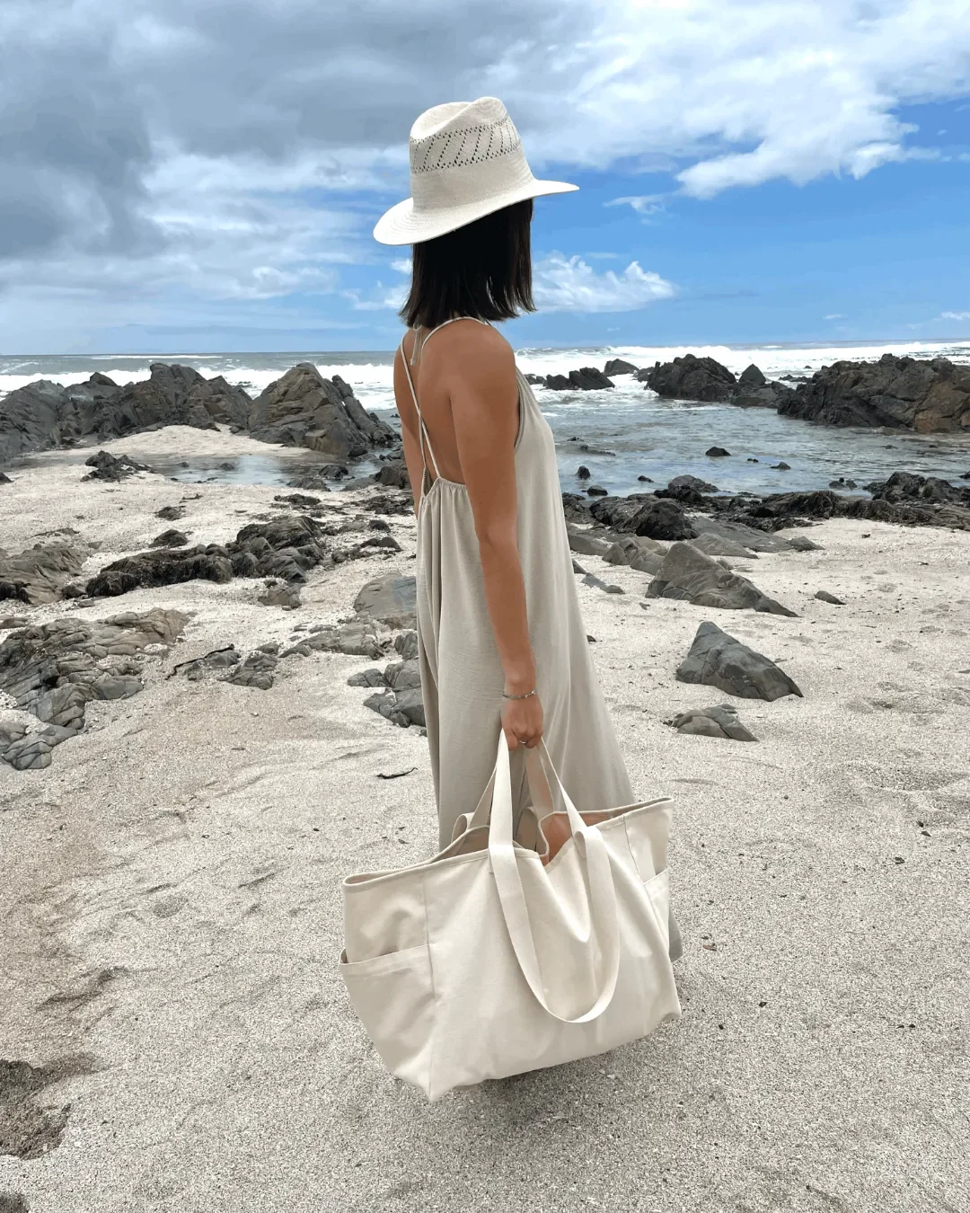 Woman on a beach carrying a large natural canvas weekending tote bag, handmade by Soli in Cape Town.