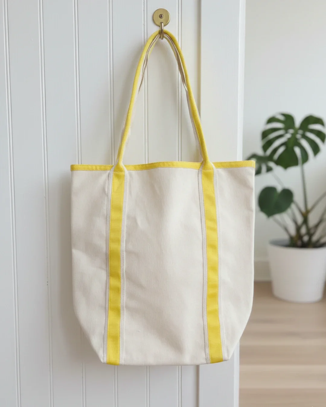 Cream heavy-weight cotton canvas Promenade bag hanging on a brass wall hook, featuring vibrant yellow vertical straps and matching top trim, handmade by Soli in Cape Town for sustainable merchandise or corporate gifts.