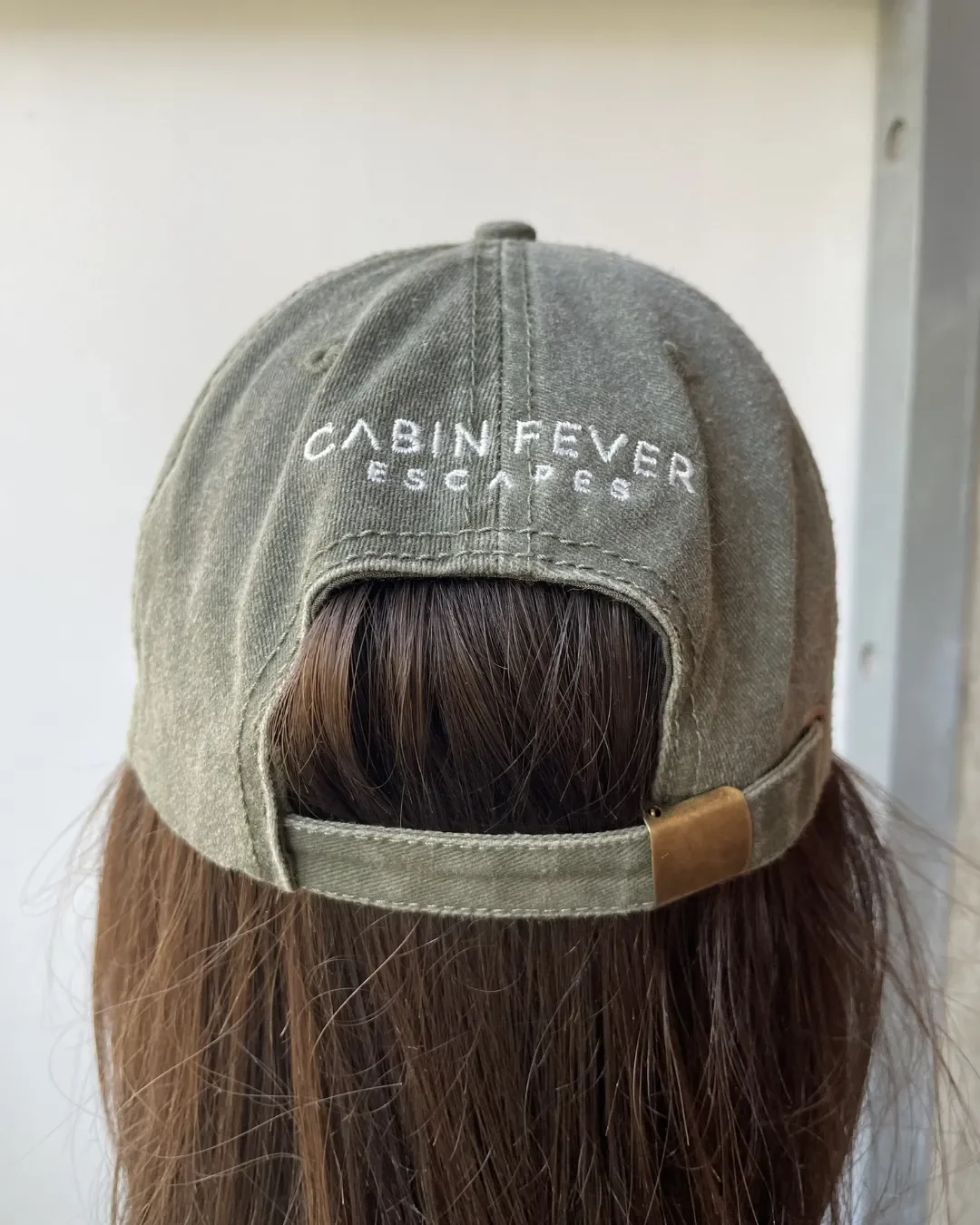 Back view of an olive green washed cotton vintage style cap featuring white custom embroidery for Cabin Fever Escapes, showing the adjustable brass buckle strap. Perfect for sustainable corporate gifting and quality merchandise, customized by local a