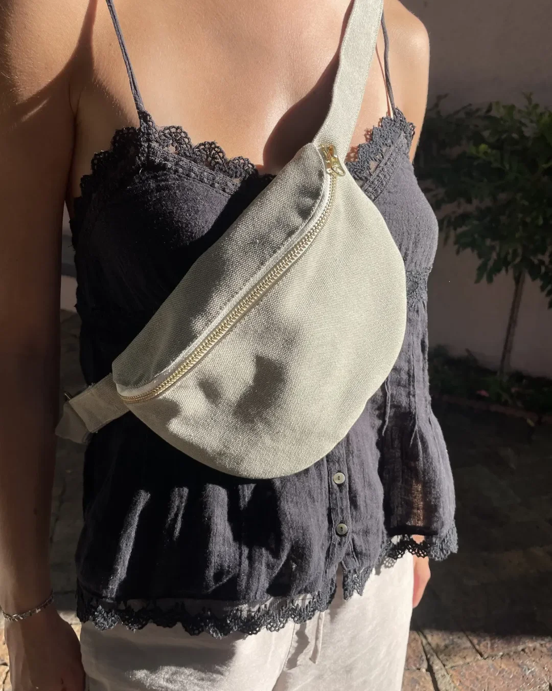 A person wearing a sage green handmade cotton canvas moon bag with a gold zipper, showcasing a sustainable and stylish fanny pack design crafted by Soli's artisans in Cape Town for corporate gifts & merchandise. 