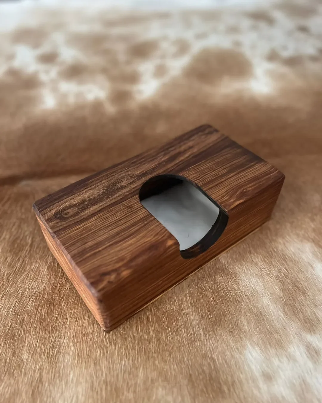 Handmade Kiaat wooden tissue box with a natural grain finish, displayed on a cowhide surface, designed for luxury hospitality and hotel room amenities, by Soli made in Cape Town. 