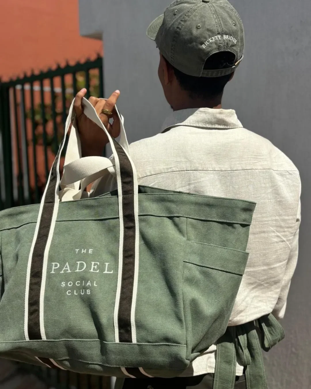 Branded olive green canvas Bush Bag with custom white printing for The Padel Social Club being carried by an artisan, Handmade by Soli in Cape Town for sustainable merchandise or corporate gifts.