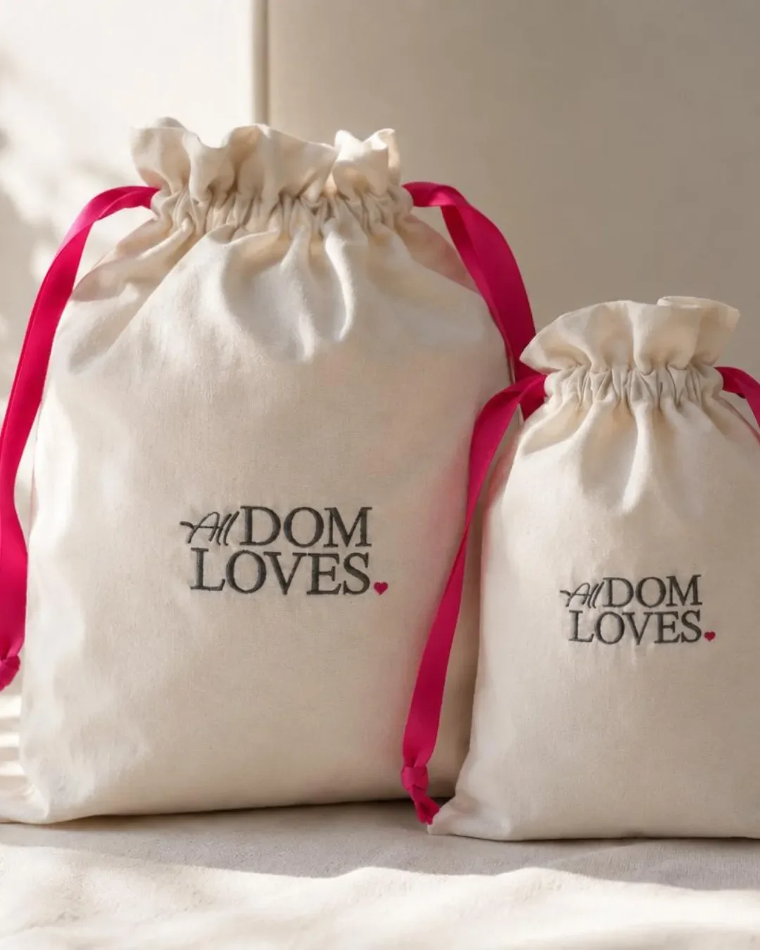 Small and medium custom embroidered cotton drawstring laundry bags with pink ribbon, handmade by Soli in Cape Town for sustainable merchandise or corporate gifts.
