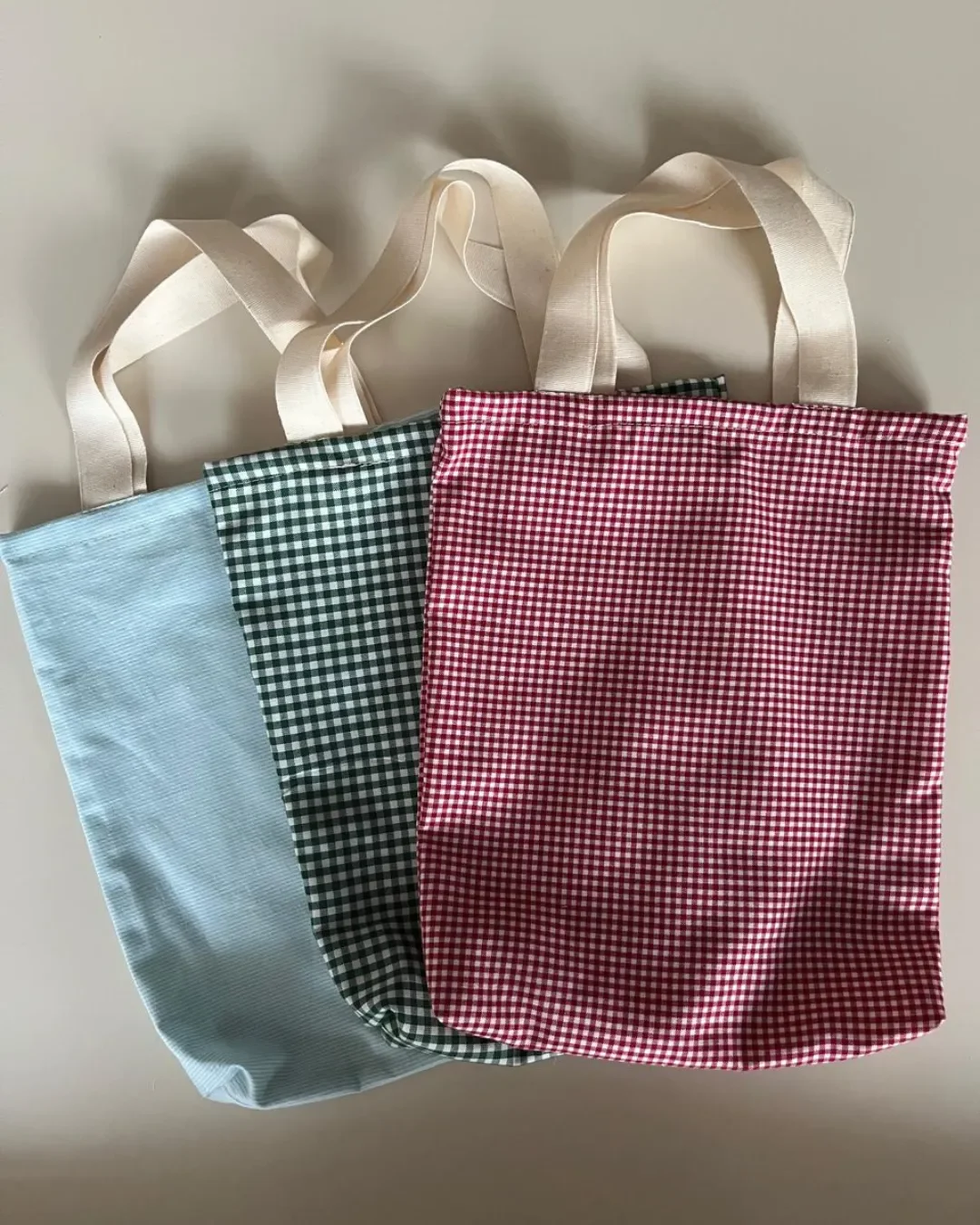 Three handmade mini tote bags in light blue, green gingham, and red gingham patterns, featuring cream cotton handles—sustainable corporate gifts for kids by Soli, made in cape town.