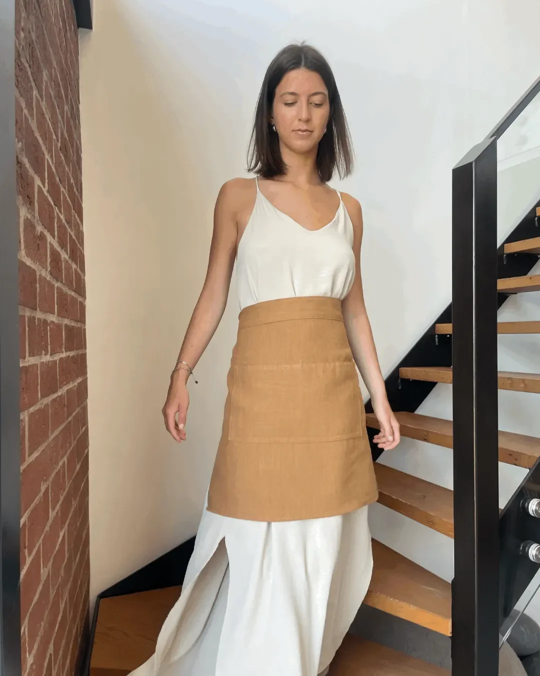 Close-up of a woman walking down stairs wearing a handmade beige calico half apron featuring professional embroidery, designed for durability in daily hospitality use.