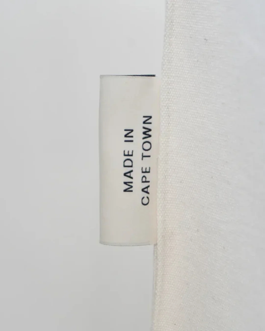 Close-up of a cream heavy canvas Doll Bag detail showing a white woven side label with black "MADE IN CAPE TOWN" text, handmade by Soli in Cape Town for sustainable merchandise or corporate gifts.