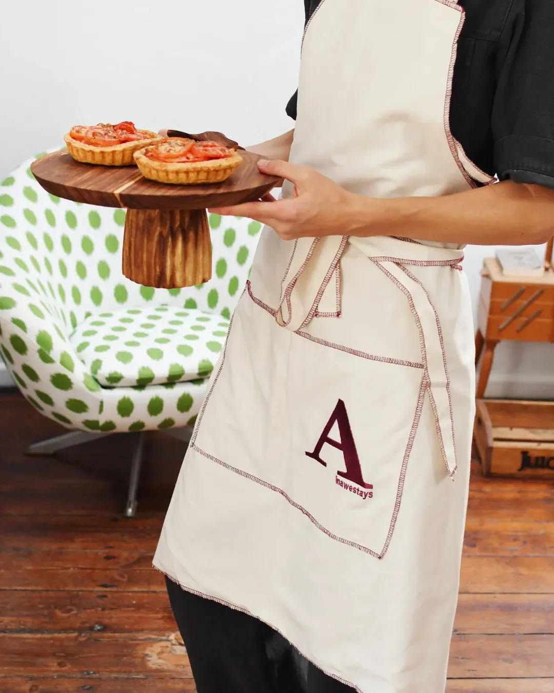 A person wearing a natural calico hospitality apron with maroon overlock edging and a custom embroidered logo, handmade in Cape Town by Soli.