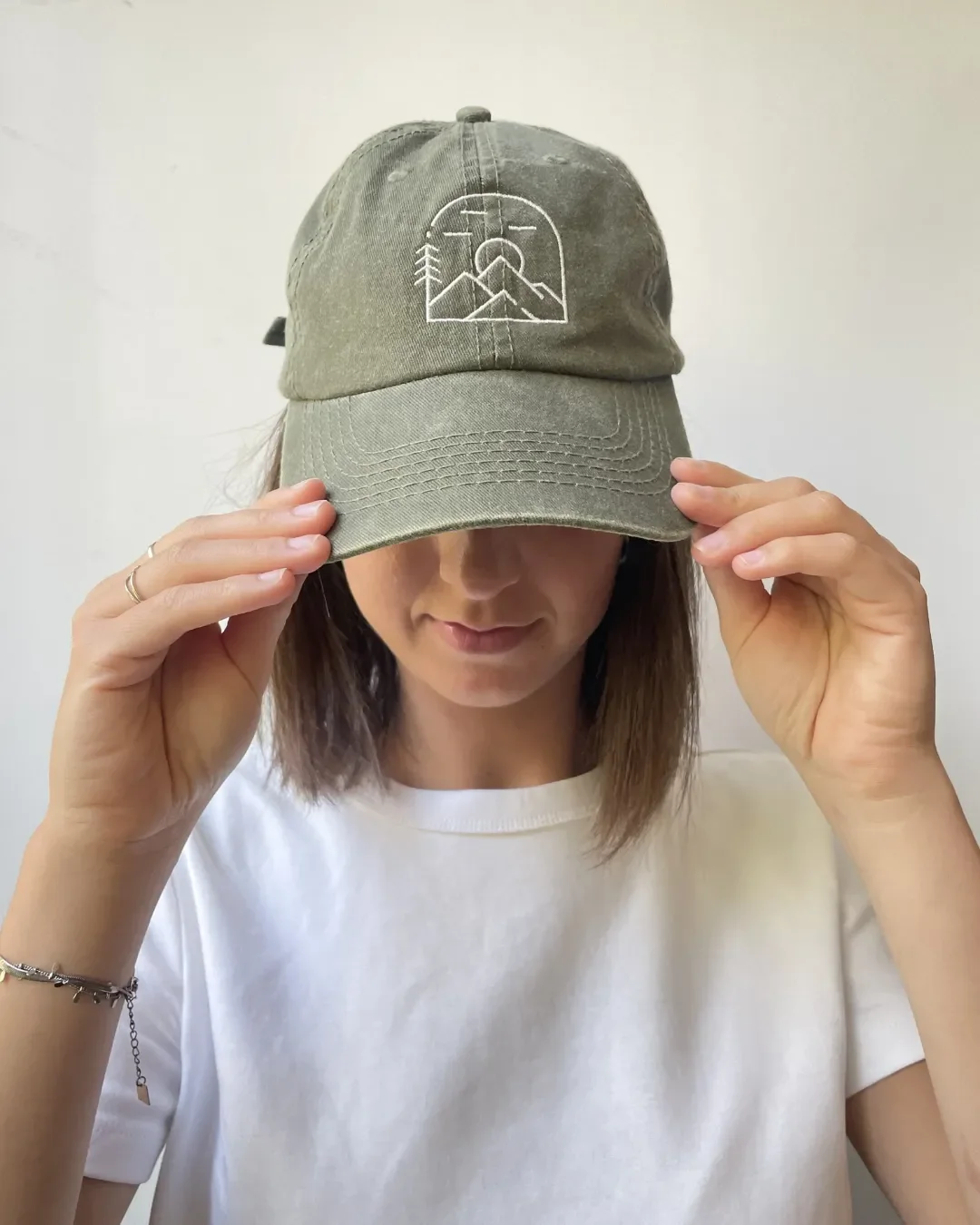 A sage olive green vintage washed cotton cap featuring a white minimalist mountain and sun embroidery, representing Soli's sustainable outdoor-themed corporate gift options.
