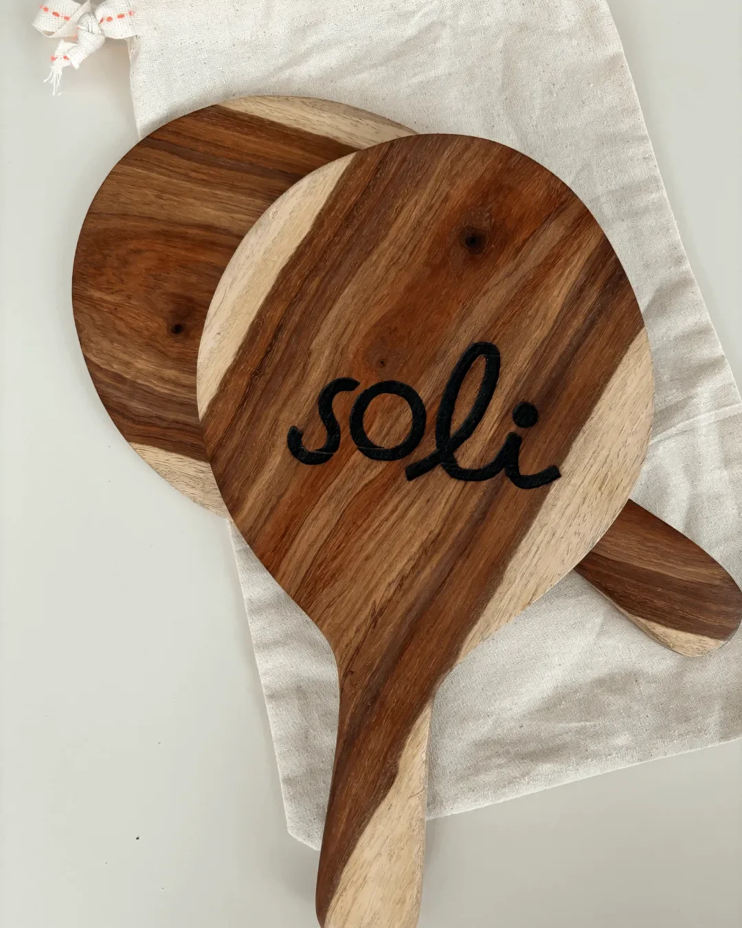 A pair of handcrafted wooden beach bats with custom black engraving on a linen drawstring bag, created by Soli in Cape Town for sustainable corporate gifting.