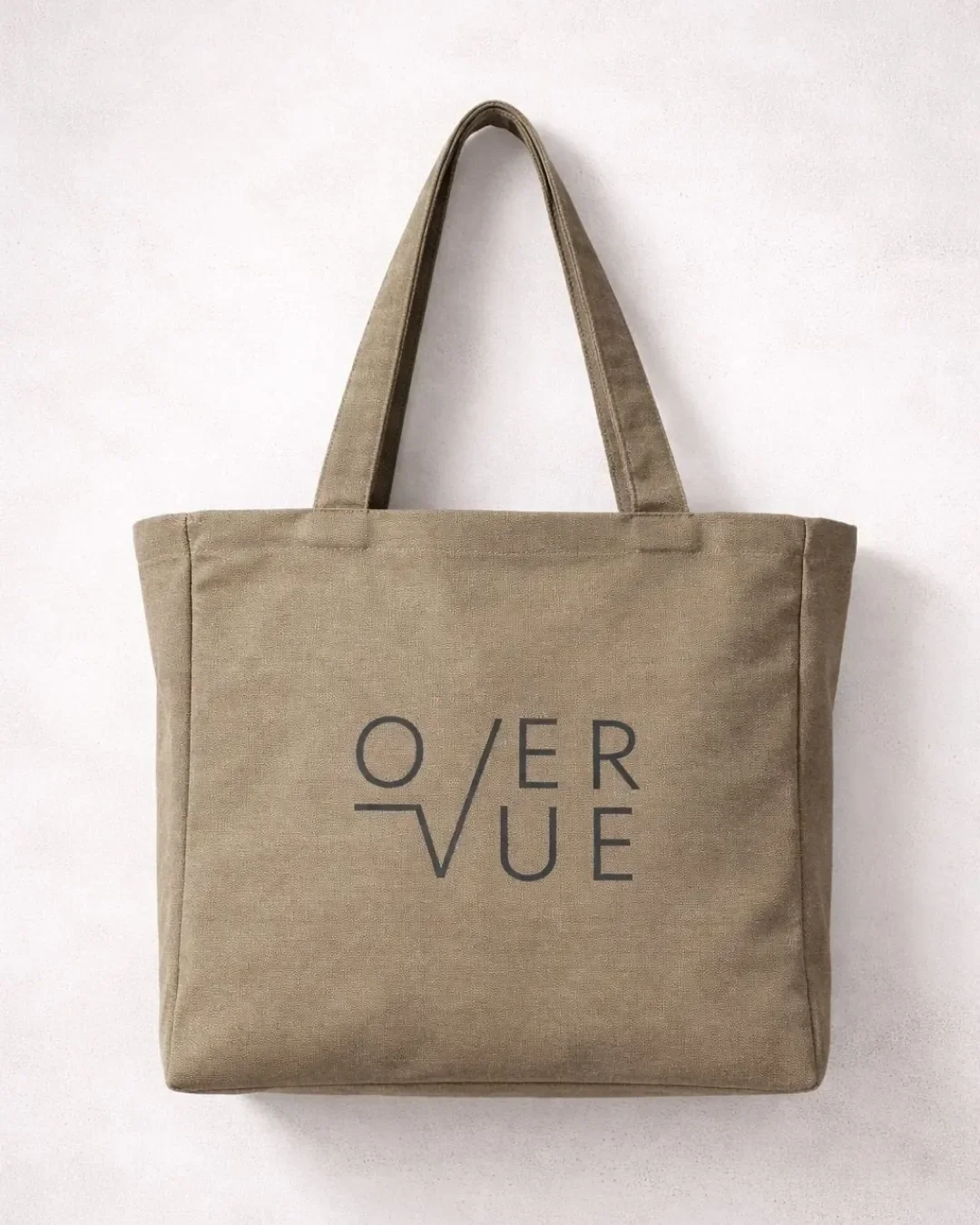 An olive green canvas corporate tote bag branded with a minimalist Overvue logo, hanging against a textured off-white wall for premium business merchandise inspiration.