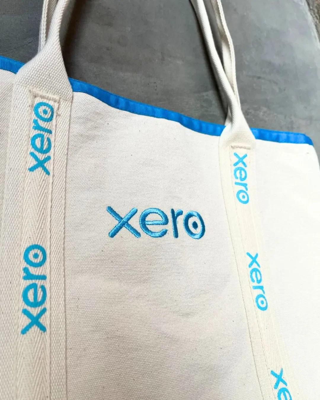 Close-up of a cream cotton canvas Promenade bag featuring vibrant blue Xero logo embroidery on the body and vertical straps, handmade by Soli in Cape Town for sustainable merchandise or corporate gifts.