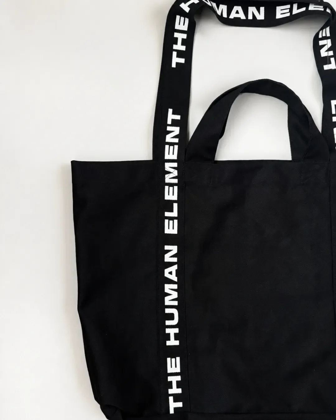 Close-up view of a custom black canvas dual carry tote bag featuring printed webbing shoulder straps and short hand handles, Handmade by Soli in Cape Town for branded merchandise or corporate gifts