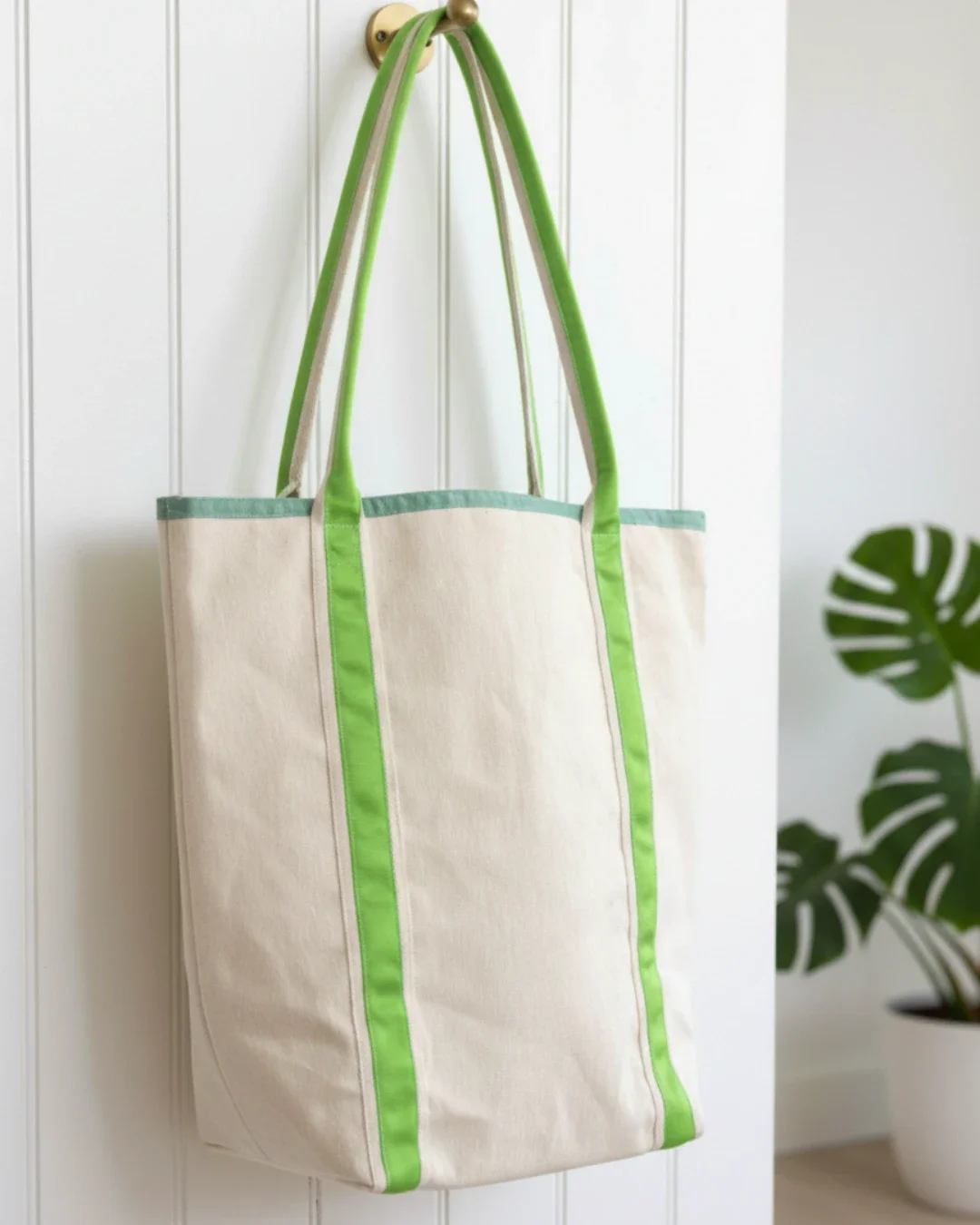 Cream heavy-weight cotton canvas Promenade bag hanging on a brass hook, featuring vibrant lime green vertical straps and a sage green top trim, handmade by Soli in Cape Town for sustainable merchandise or corporate gifts.