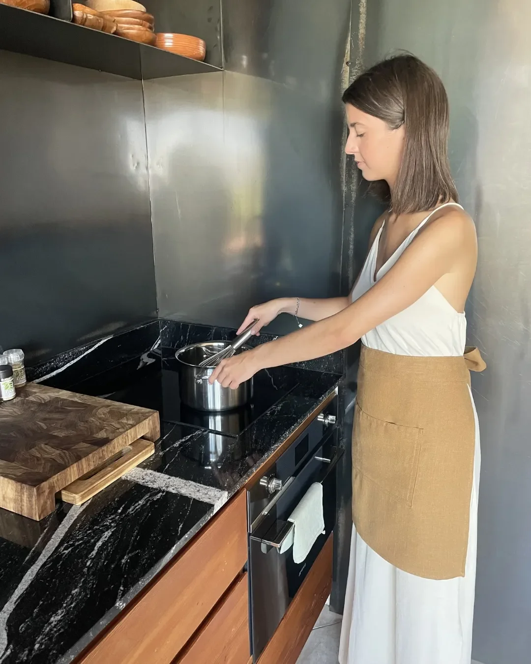 A woman in the kitchen wearing a natural beige calico half apron with a custom printed logo, handmade in Cape Town for sustainable hospitality branding.
