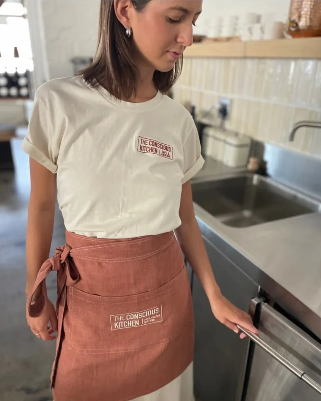 A person wearing a terracotta-colored custom canvas hospitality apron with a printed logo, handmade by local artisans in Cape Town, for branded hospitality aprons made by Soli.