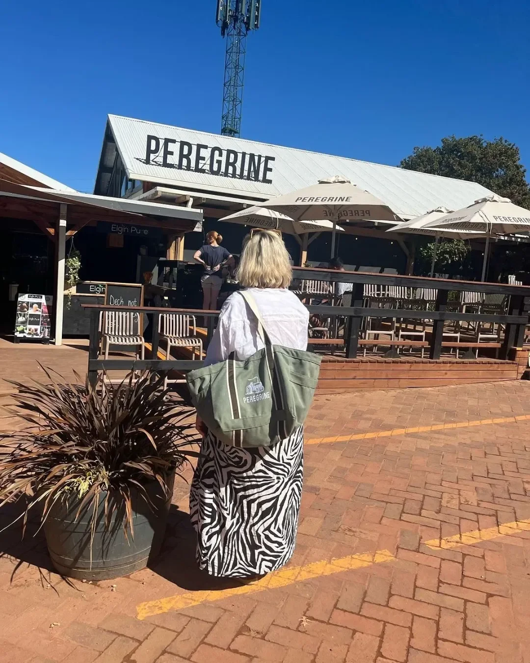 A person carrying a branded olive green canvas Bush Bag with a custom Peregrine logo at an outdoor venue, Handmade by Soli in Cape Town for sustainable merchandise or corporate gifts.