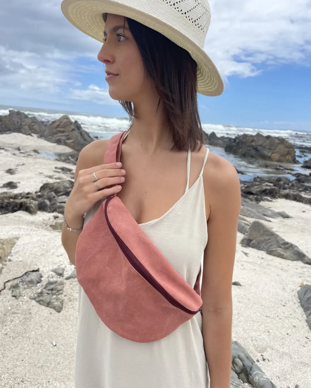 A woman on a beach wearing a terracotta-colored canvas moon bag across her chest, handmade by Soli in Cape Town