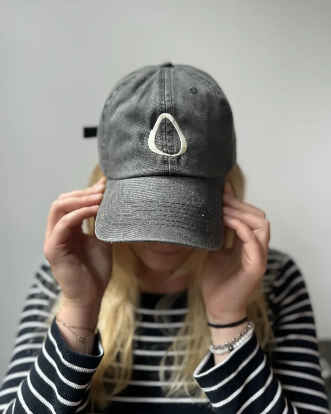 A person wearing a charcoal grey vintage-style washed cotton cap with a white embroidered logo, representing Soli’s custom sustainable corporate gift range in South Africa.