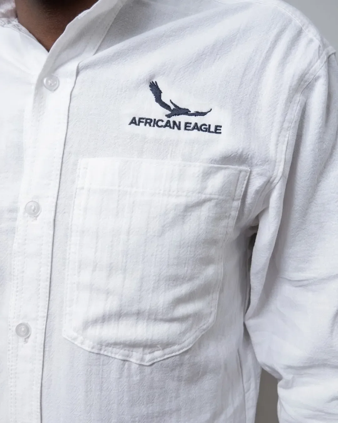 Close-up detail of crisp logo embroidery above the chest pocket on a white custom shirt, Handmade shirts by Soli in Cape Town for staff merchandise.