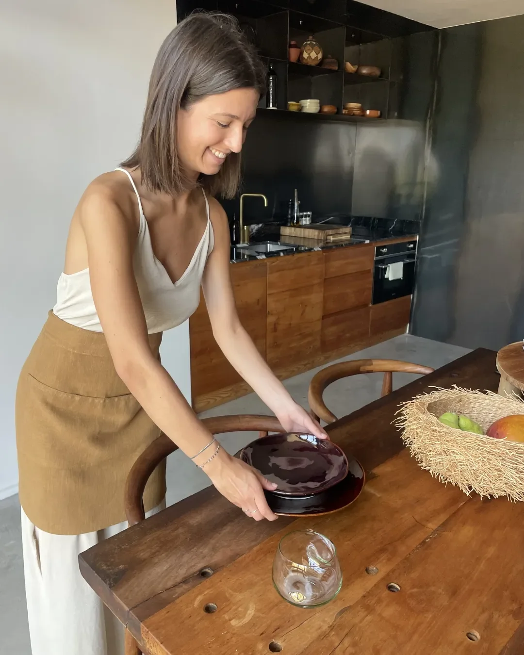 A woman in the kitchen wearing an artisan-made beige calico half apron produced from locally sourced, sustainable calico material, made in Cape Town by Soli.