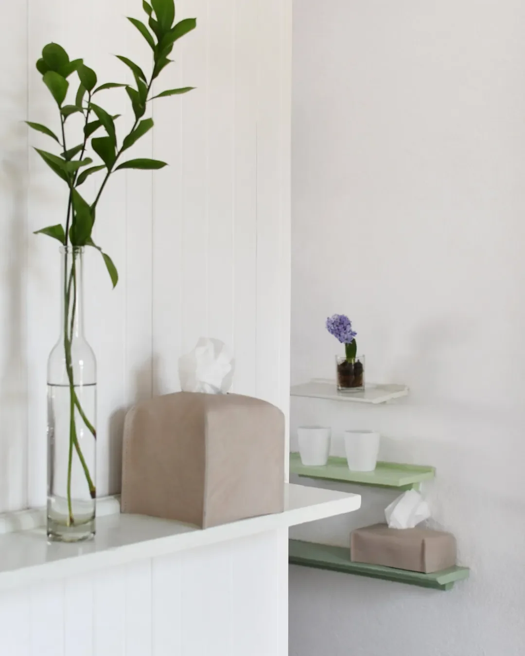 Handmade square and rectangular leather tissue box covers in a neutral beige tone, displayed in a minimalist white interior for luxury hospitality amenities. By Soli, Made in Cape Town.