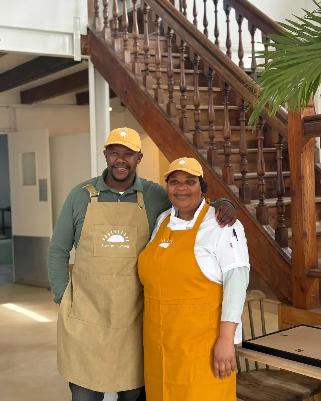 Two hospitality staff wearing custom branded canvas full-body aprons with embroidered logos, handmade by local artisans in Cape Town by Soli.