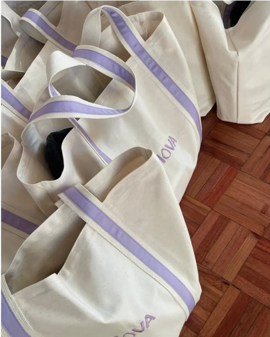 Bulk order of custom Milano Tote bags in heavy cream canvas featuring lilac purple handles and embroidered branding, handmade by Soli's artisans in Cape Town for merchandise or corporate gifts.