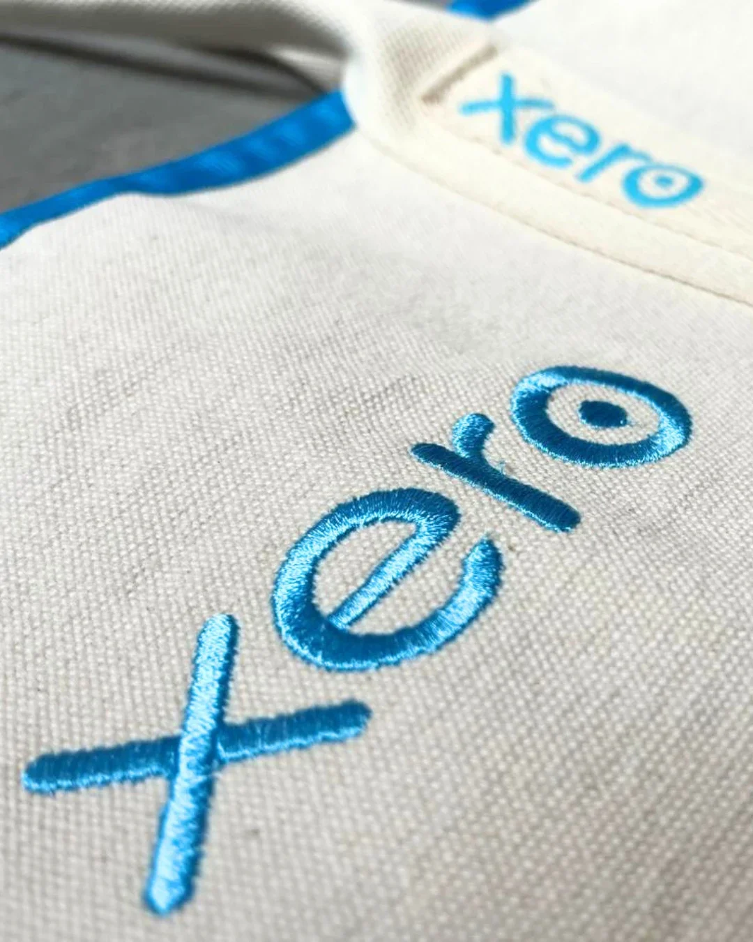 Extreme close-up showing the high-quality blue thread embroidery of the Xero logo on a cream 100% cotton canvas Promenade bag, handmade by Soli in Cape Town for sustainable merchandise or corporate gifts.