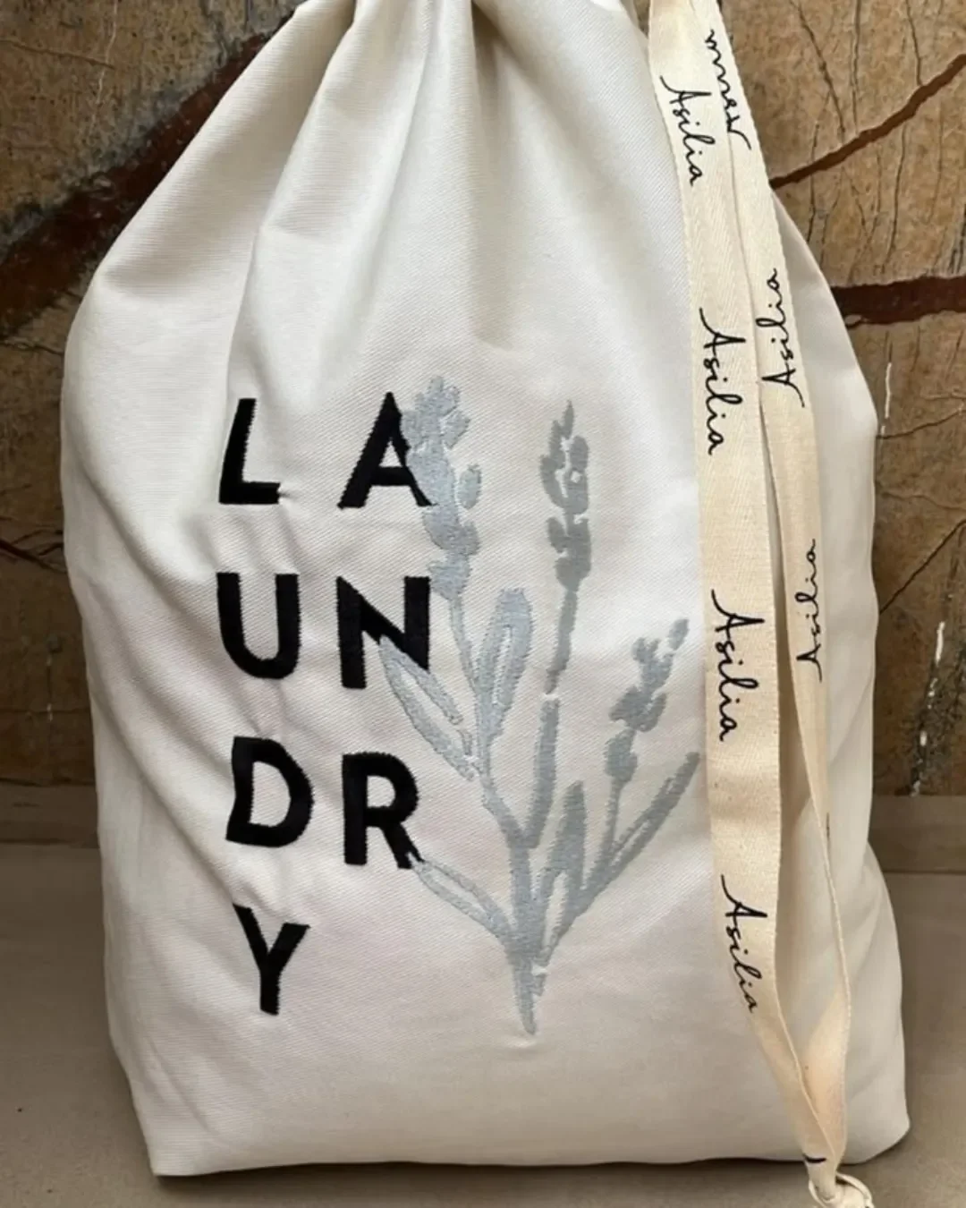 Custom branded off-white cotton hotel laundry bag with black bold text, botanical print, and printed Asilia ribbon drawstring by Soli Cape Town