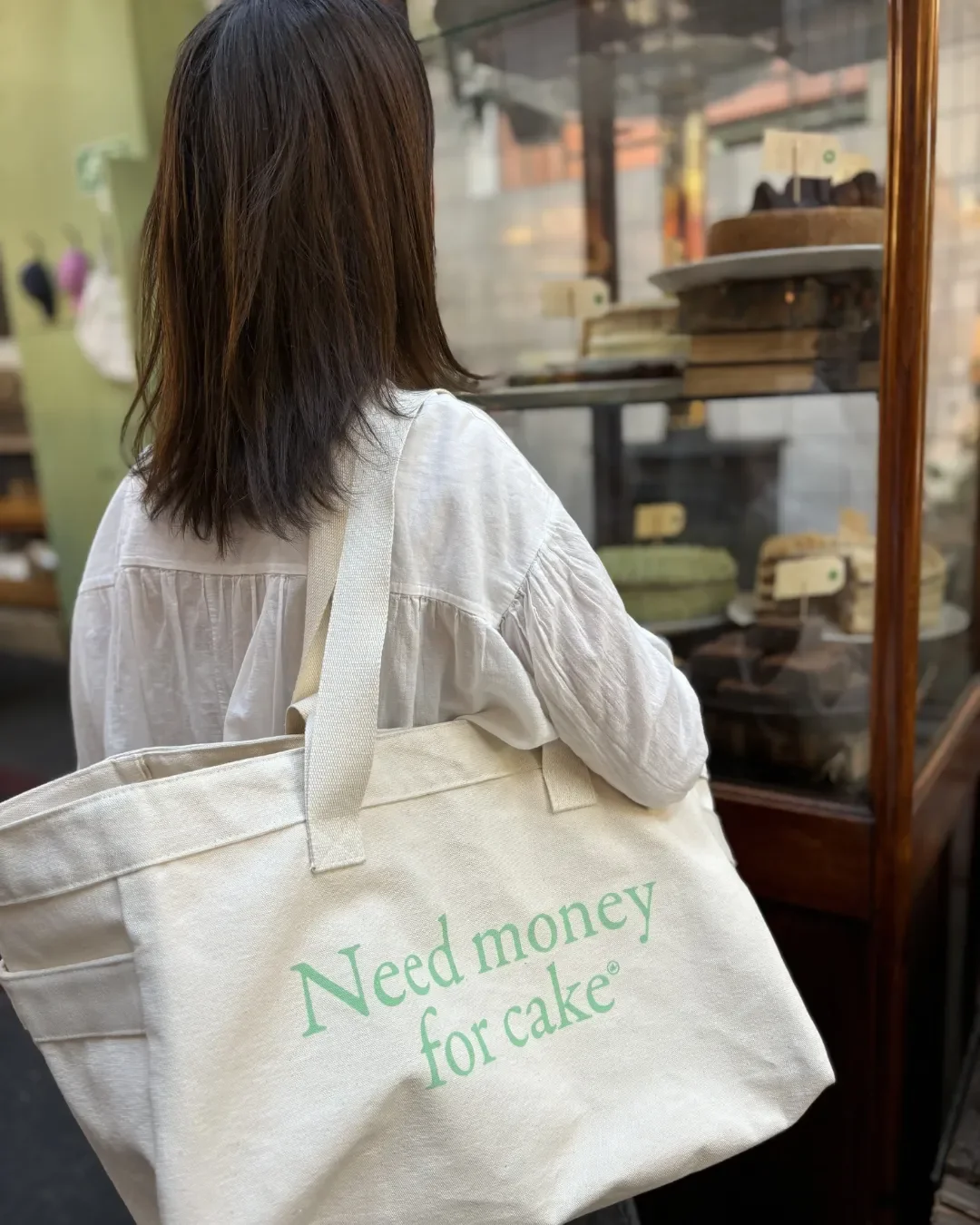 A person carrying a large cream 100% cotton canvas Weekending Bag with 'Need money for cake' printed in green, Handmade by Soli in Cape Town for merchandise or corporate gifts.