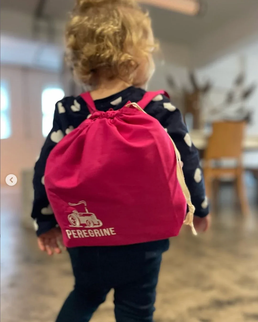 A child wearing a bright pink handmade drawstring mini backpack with a white printed logo, designed by Soli as a sustainable corporate gift for kids, made in Cape Town.