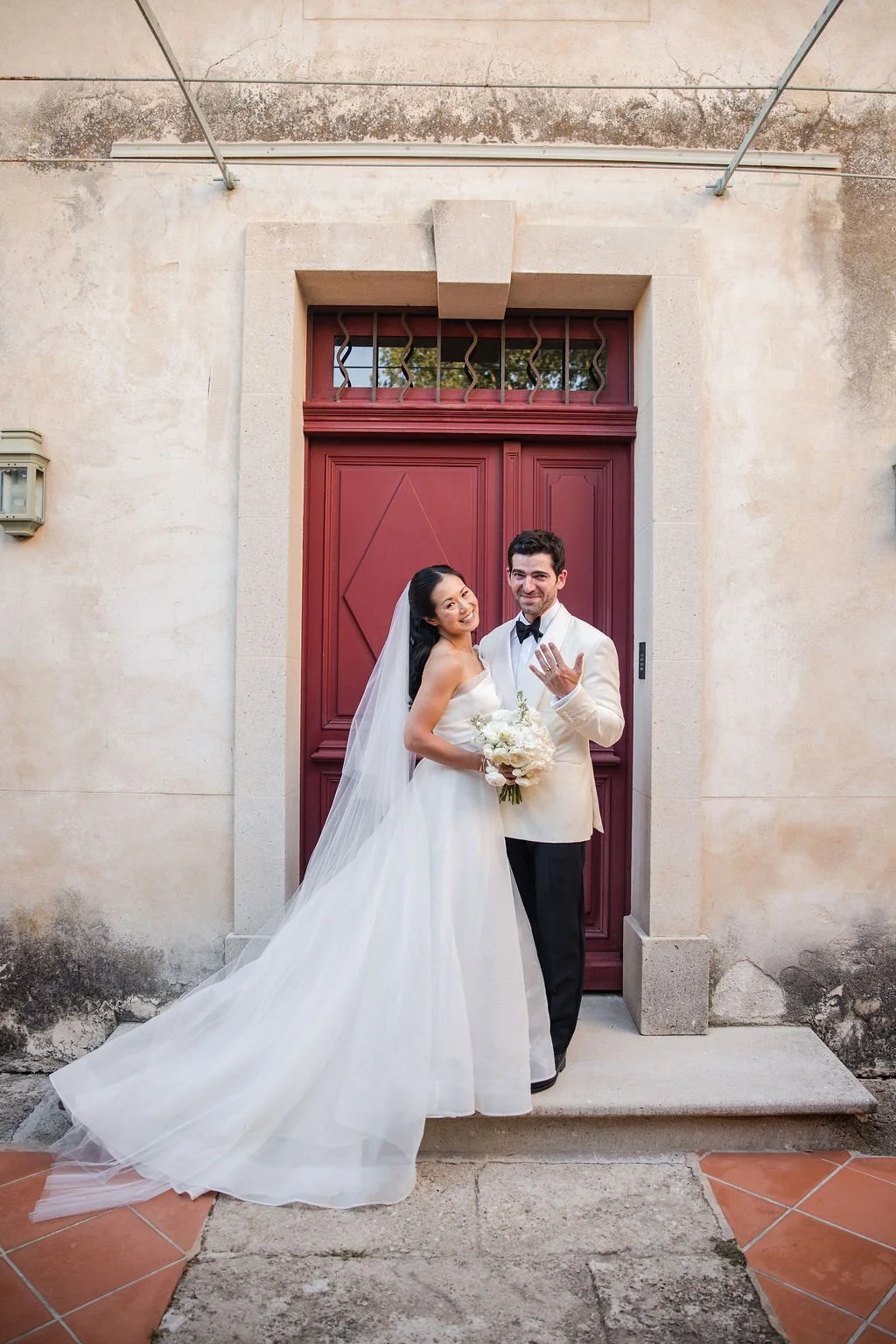 Newlyweds laughing in front of a red château door after their wedding at Château de Beauregard, Provence, France