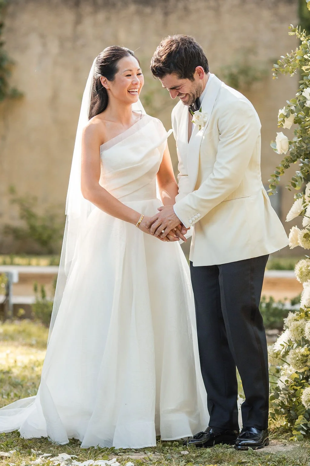 Bride and groom holding hands during their outdoor wedding ceremony among white flowers at Château de Beauregard, Provence