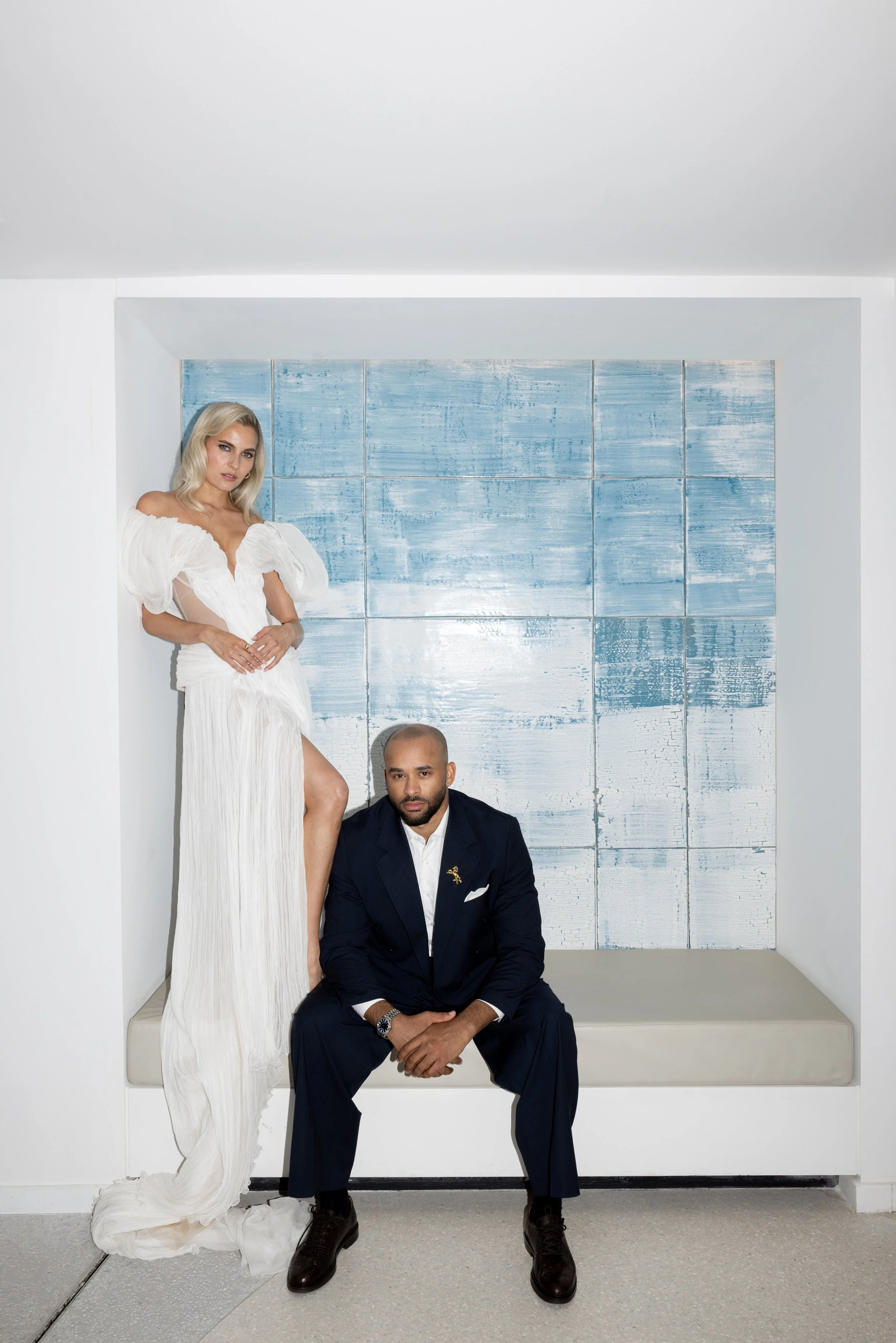Bride standing beside the seated groom in front of a pale blue artwork at The Maybourne Riviera, sculptural bridal beauty by Mathilde Vintze