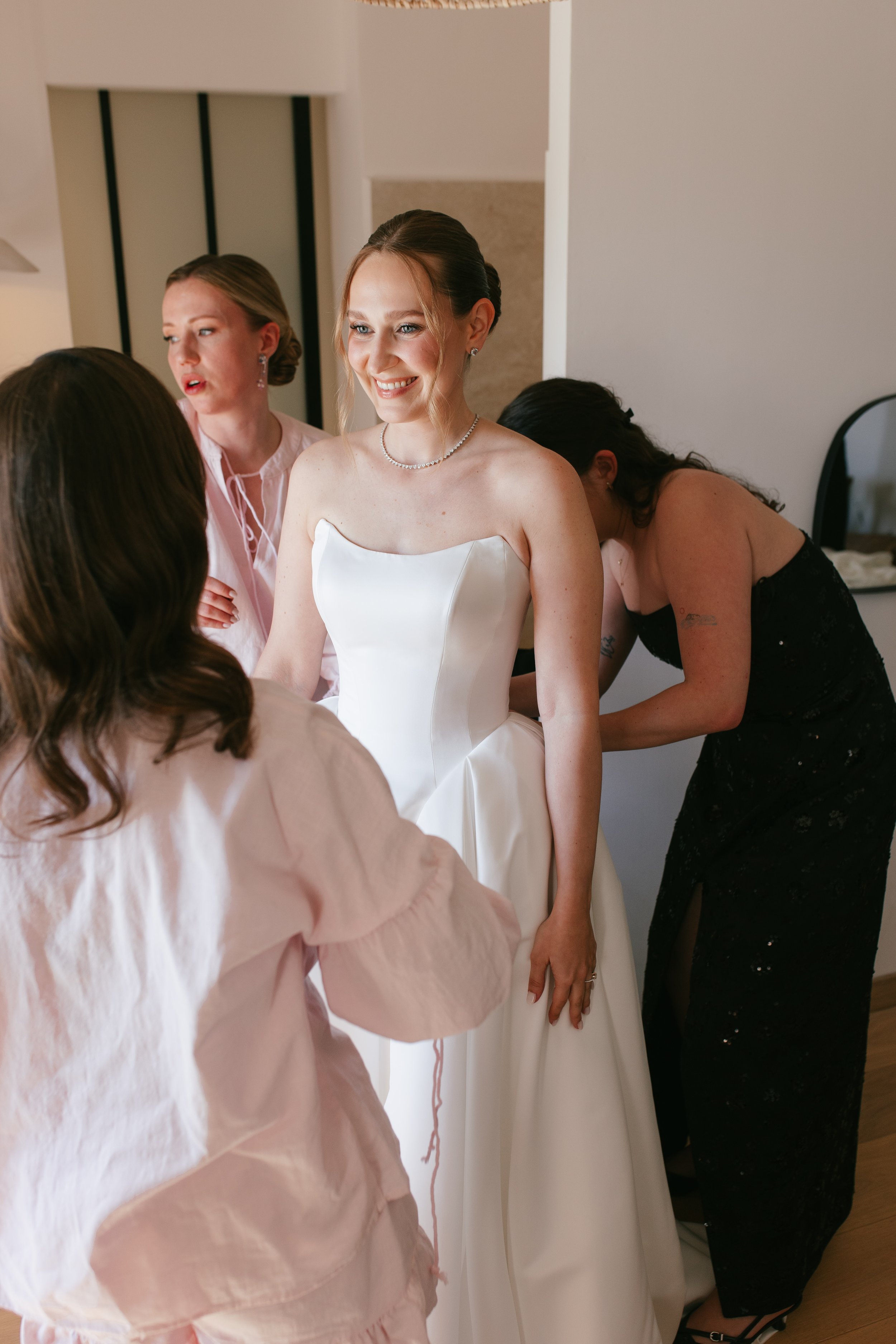 Bridal preparation moment as the bride gets ready surrounded by her bridesmaids, showcasing flawless wedding-day makeup and styling by Mathilde Vintze Artistry.