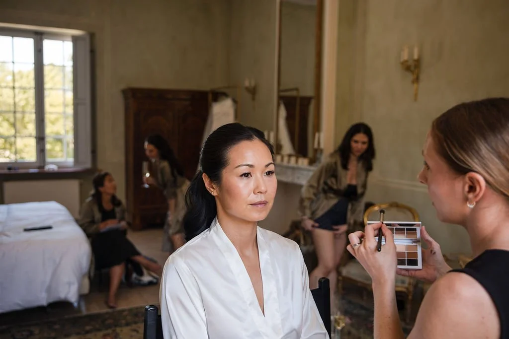 Bride in a white satin robe during her wedding-morning bridal makeup at Château de Beauregard, Provence, by Mathilde Vintze