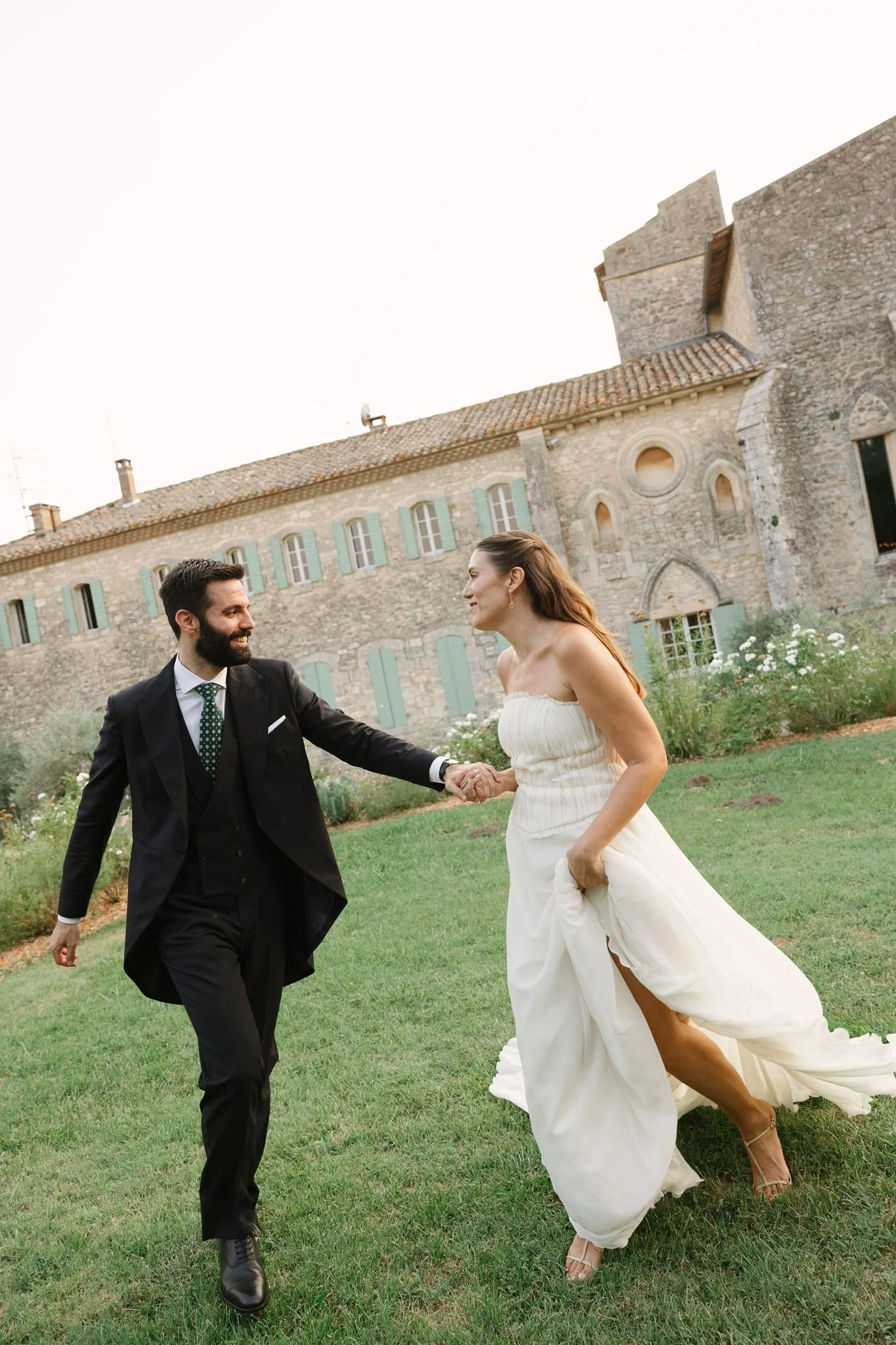 Bride and groom running hand in hand across the lawn of the Couvent Notre-Dame des Prés, Provence
