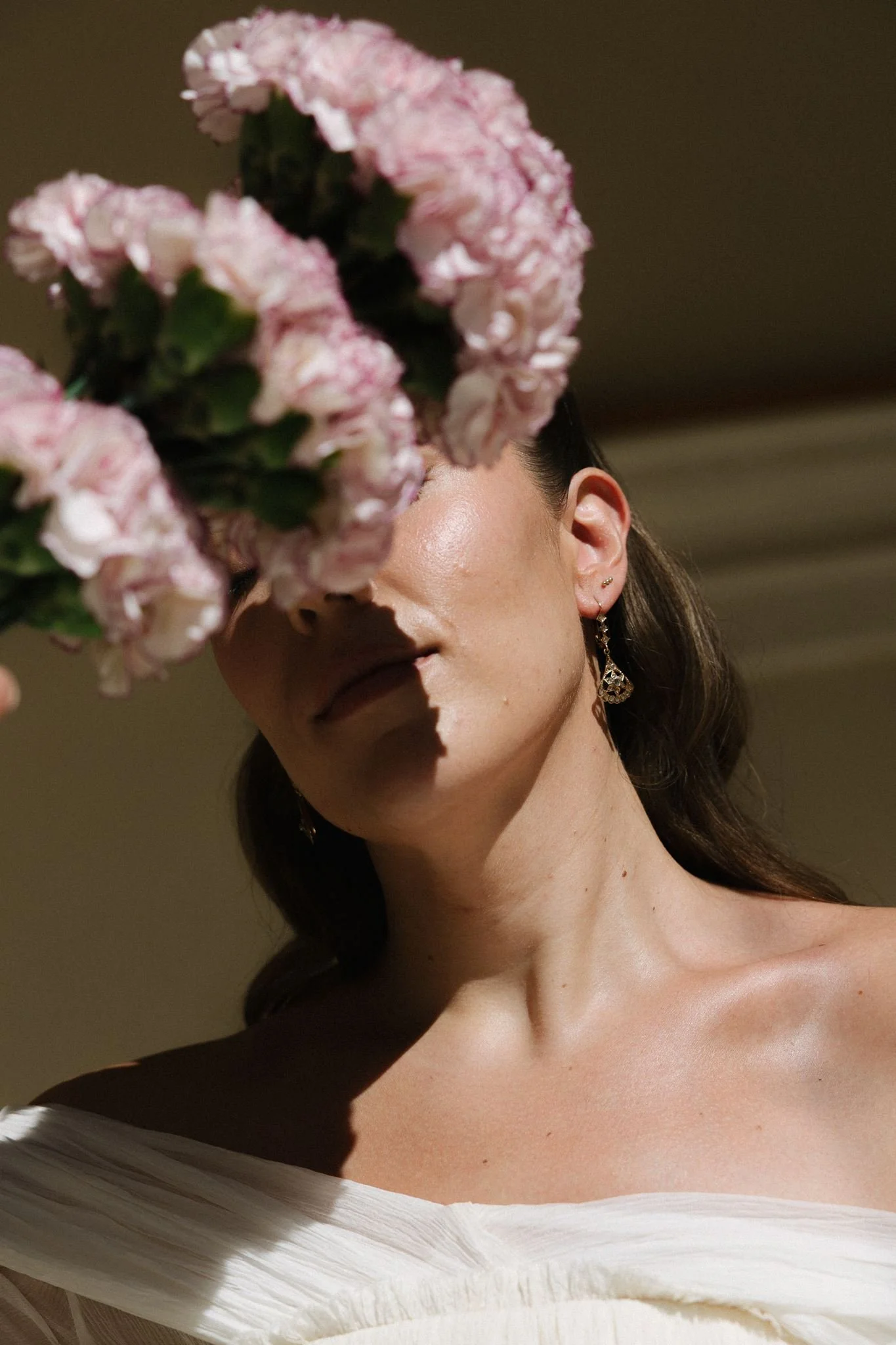 Close-up of the bride’s luminous skin and natural bridal makeup, her face partly hidden by pink carnations