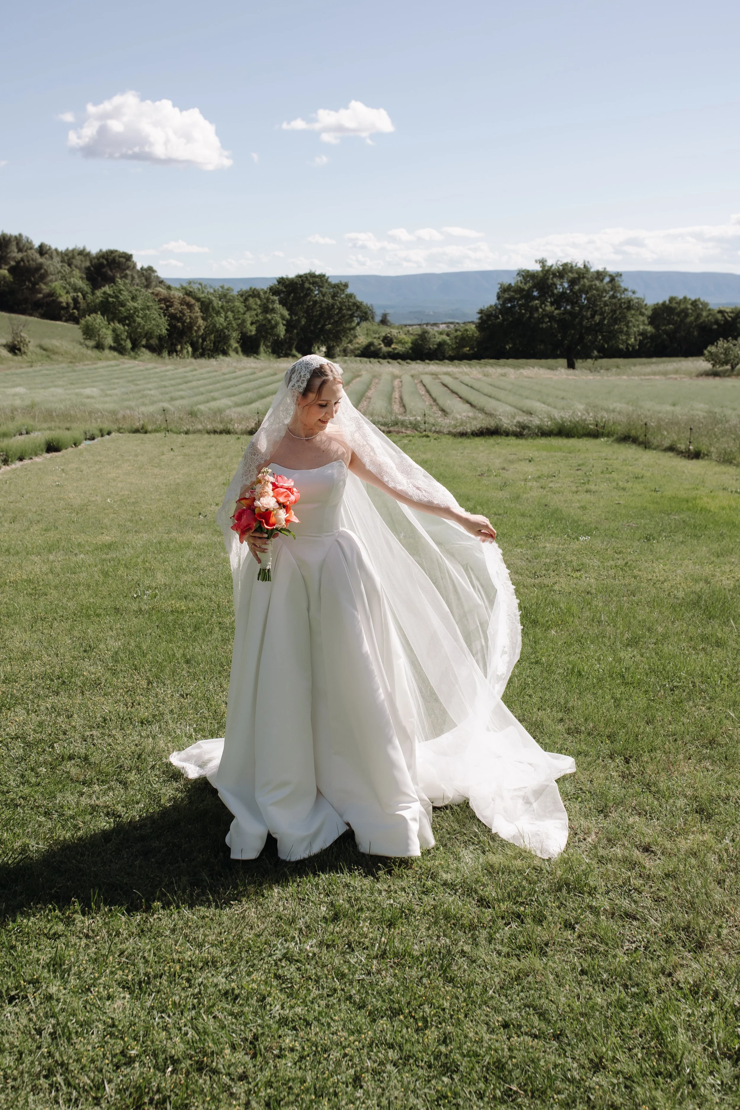 Outdoor bridal portrait featuring soft natural wedding makeup and an elegant updo by Mathilde Vintze Artistry. Romantic countryside bride in a flowing white gown holding a colourful bouquet.