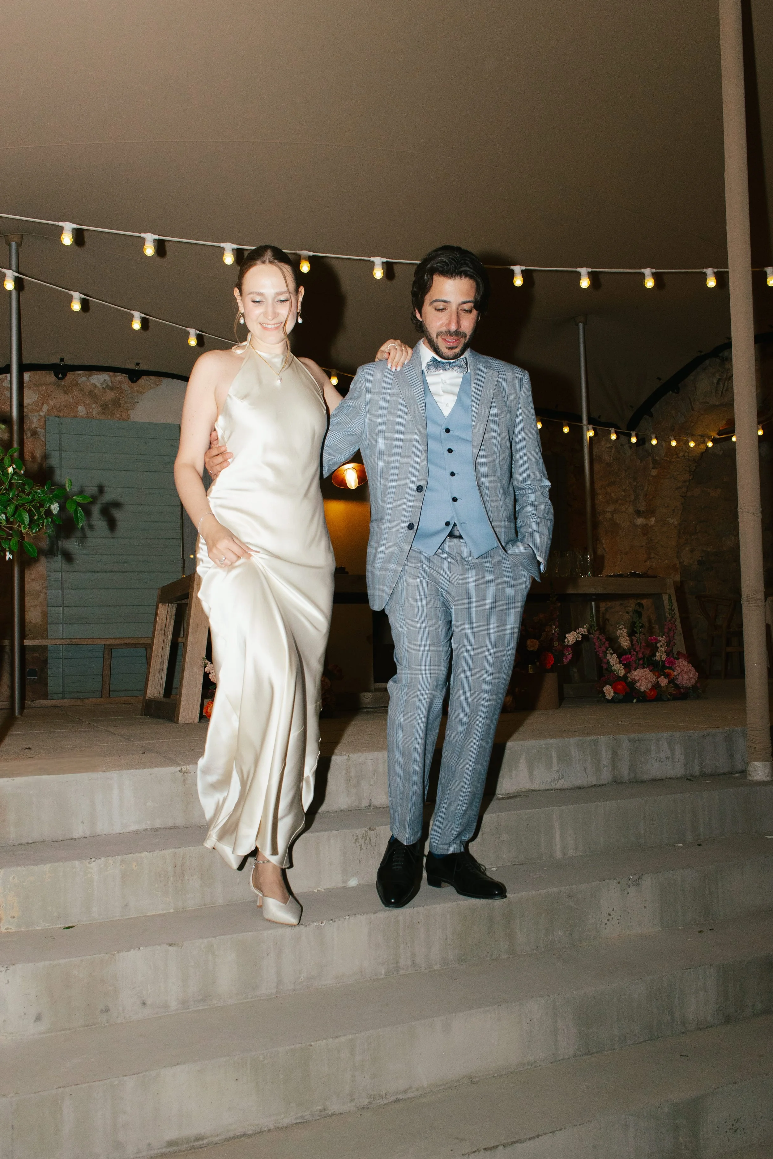 Evening wedding reception portrait of the newlyweds under string lights, the bride glowing with elegant soft-glam makeup by Mathilde Vintze Artistry.
