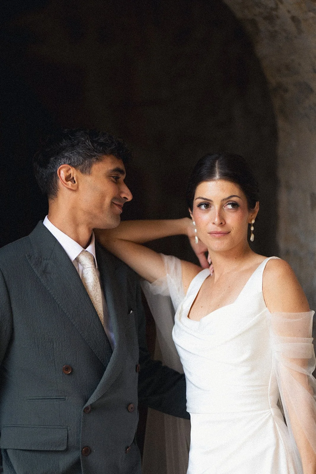 Bride and groom portrait at Couvent Notre-Dame des Prés in Provence, the bride resting her arm on the groom's shoulder. Luminous, natural bridal makeup with a softly sculpted complexion and sleek low bun.