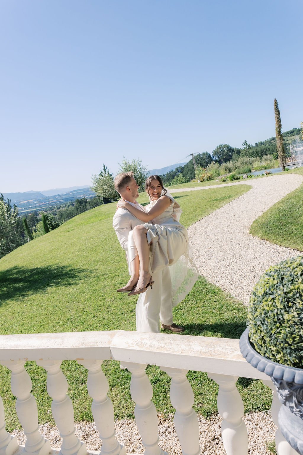 Groom carrying his bride in a Provence garden overlooking the hills, the bride glowing with long-lasting natural wedding makeup by Mathilde Vintze