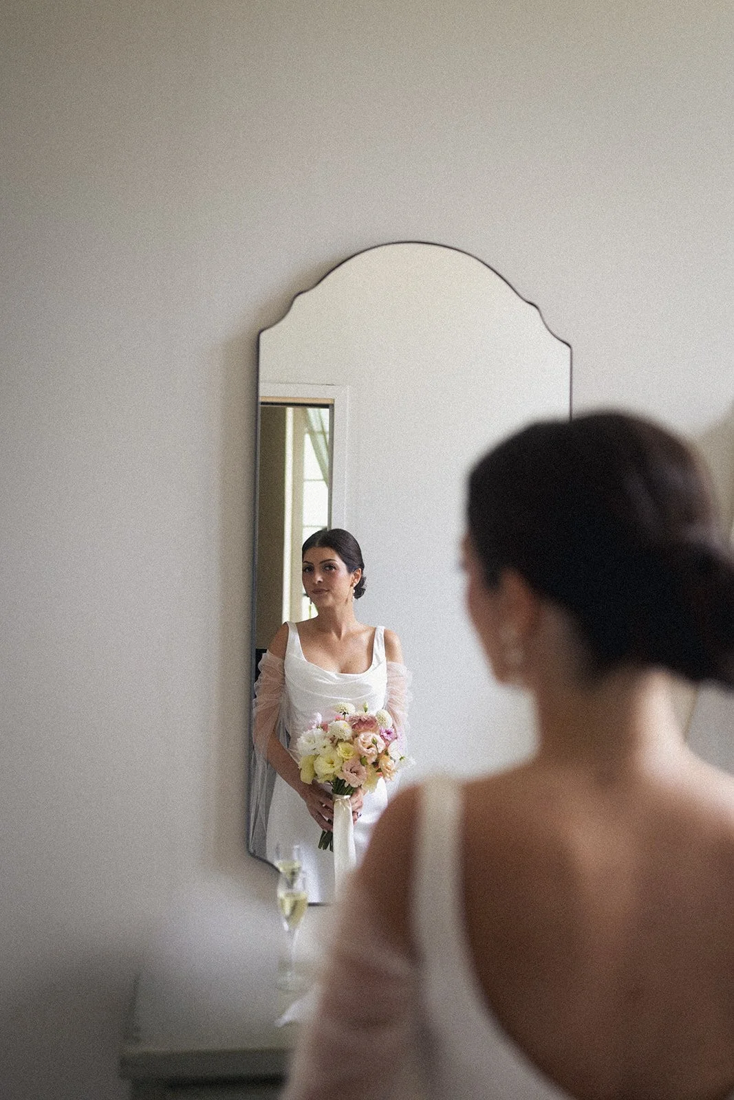 The bride sees her finished look in the mirror, bouquet in hand. Elegant, understated bridal makeup for a summer wedding in Provence.