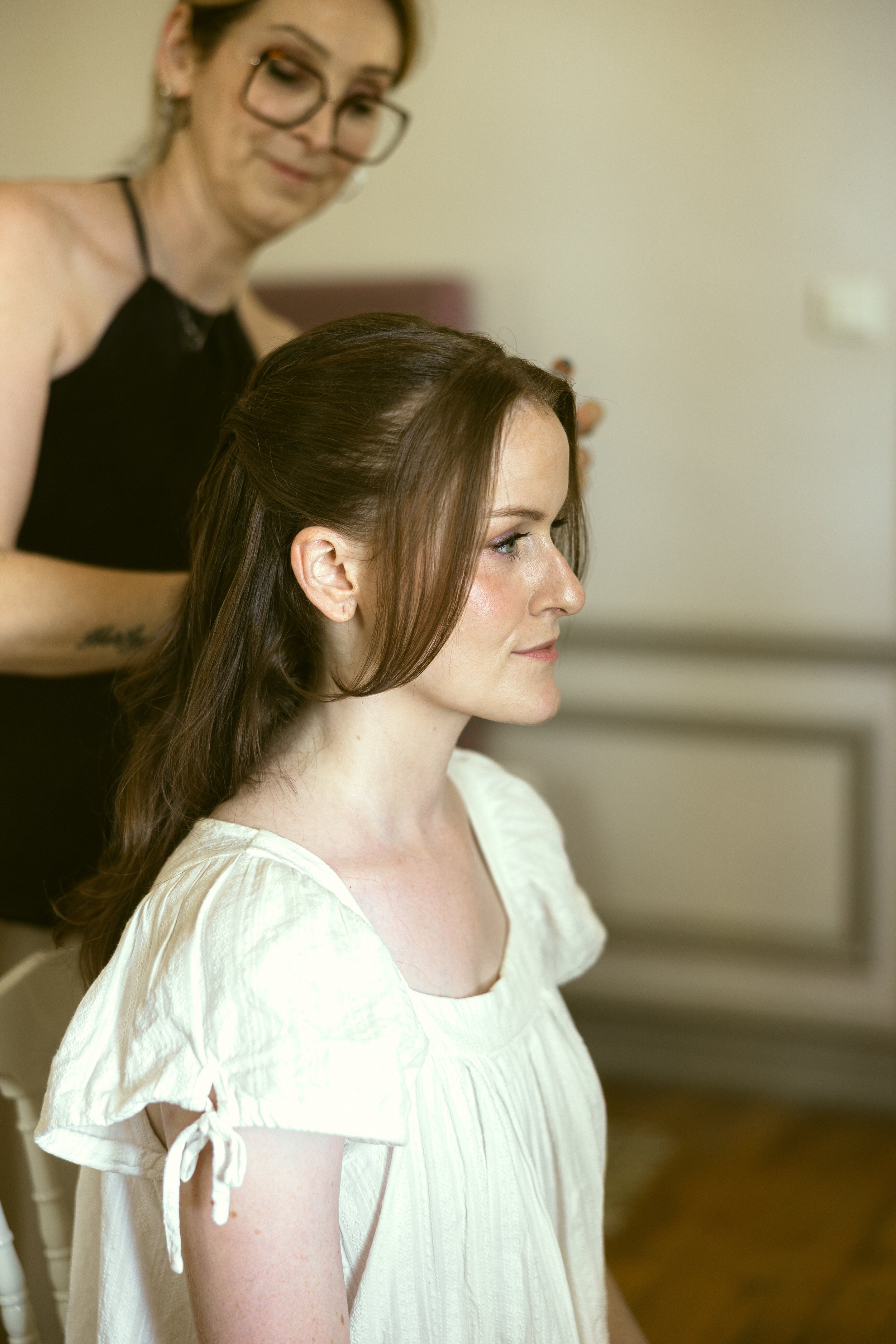 Bridal getting-ready moment: The bride has her soft half-up wedding hairstyle finished, wearing fresh, skin-first bridal makeup designed to reveal her natural features.