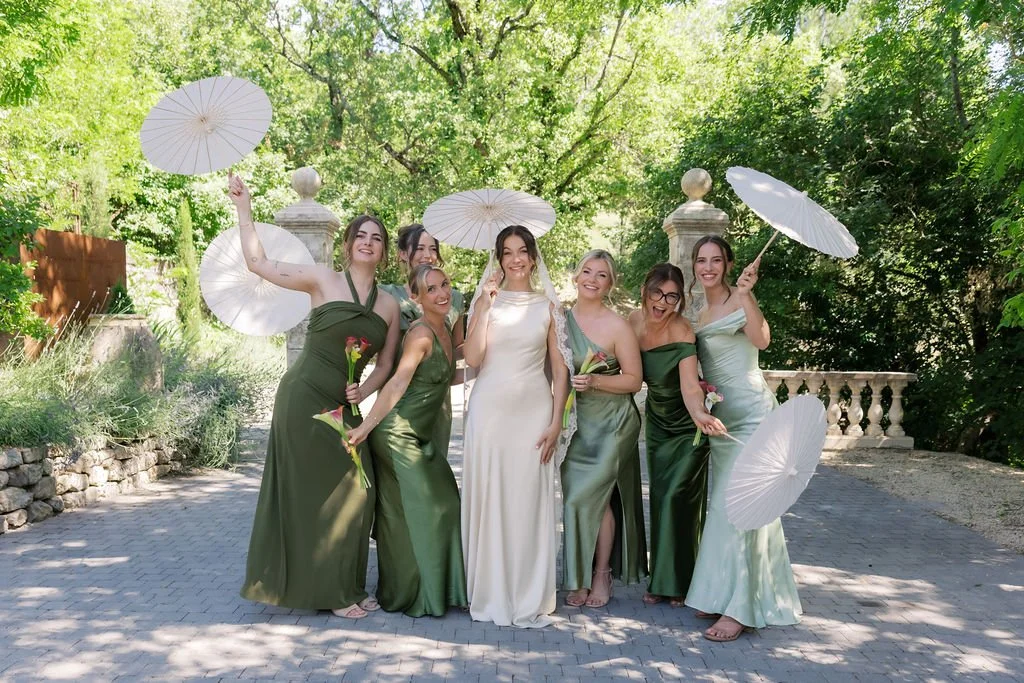 Bride with her bridesmaids in green gowns holding lace parasols in a Provence garden, bridal party makeup by Mathilde Vintze