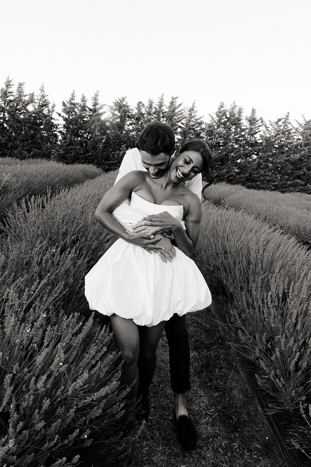 A couple smiling and embracing in a field of tall plants, in black and white.